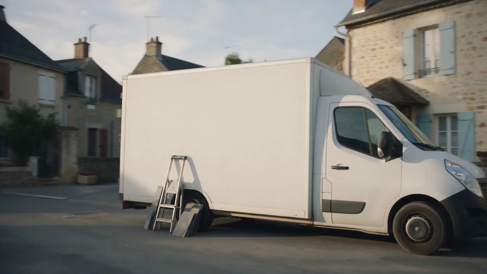 Une camionnette blanche garée dans une rue d'un petit village français, son flanc laissé vierge, prête à être trouvée.